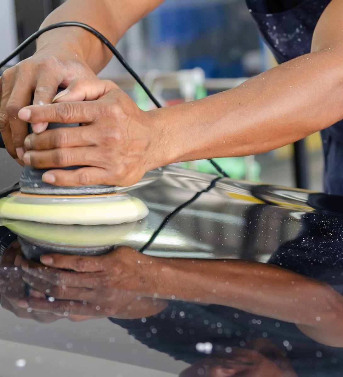 Detailer's hands hand-polishing a glossy black car exterior with a buffer
